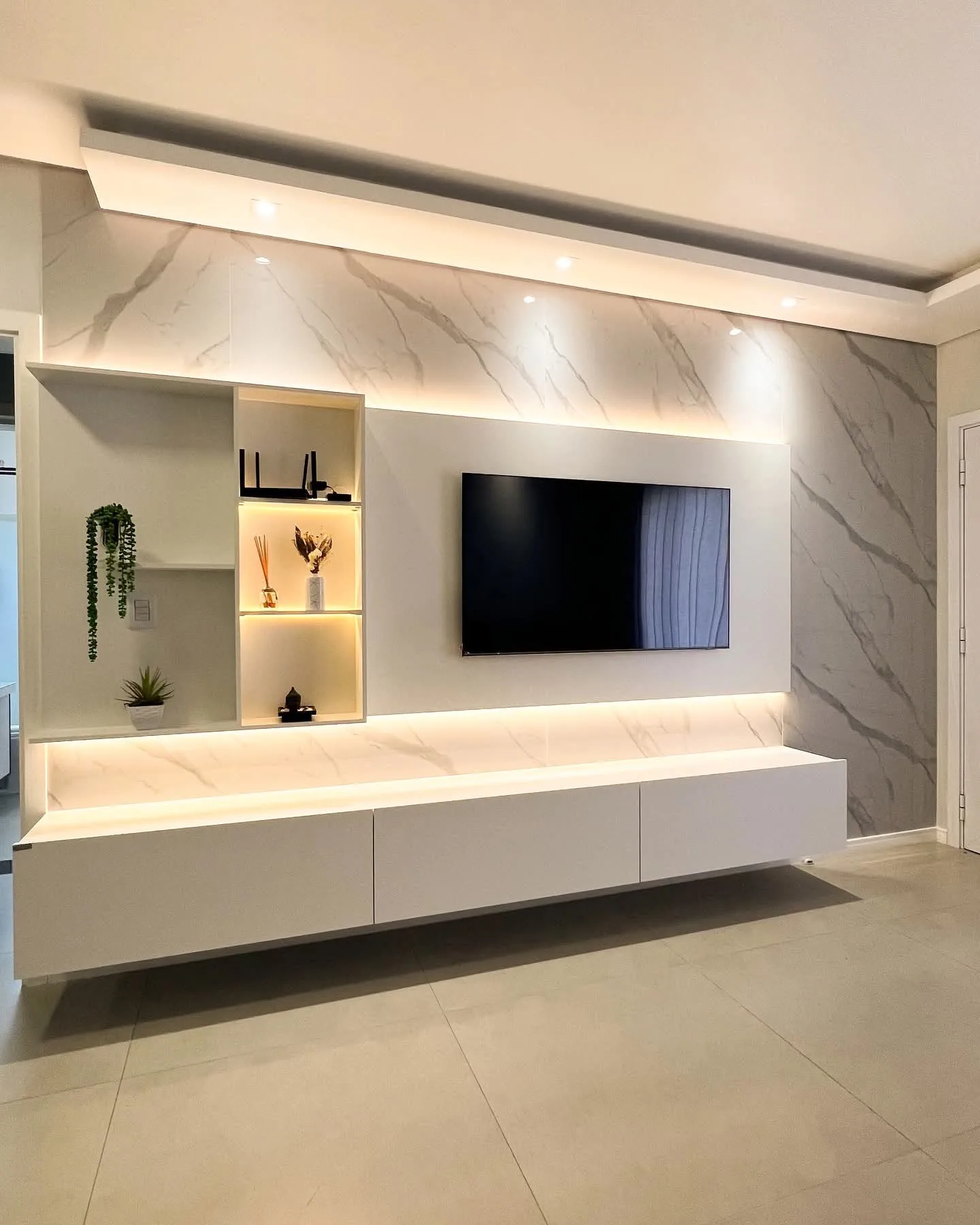 Sala planejada com painel de televisão, nichos iluminados e armário suspenso